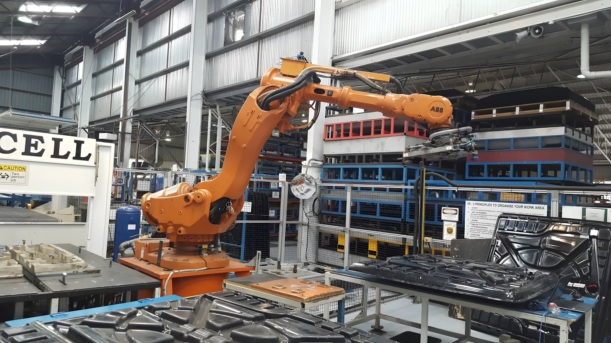 Six-axis ABB robot lifting moulded automotive panels in a robotic handling cell